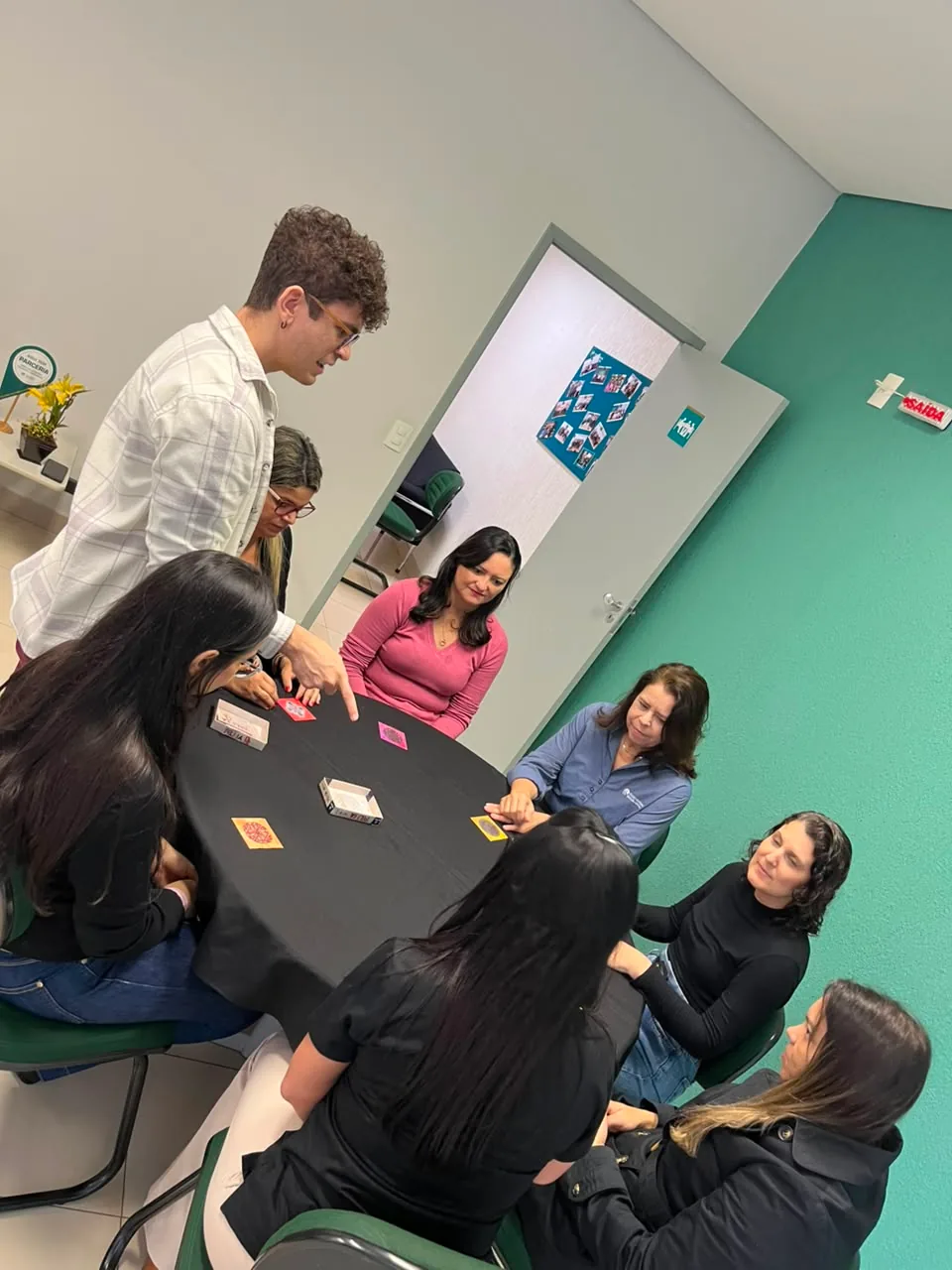 Grupo em volta de uma mesa jogando um jogo de cartas, concentrado nas jogadas, durante a confraternização
