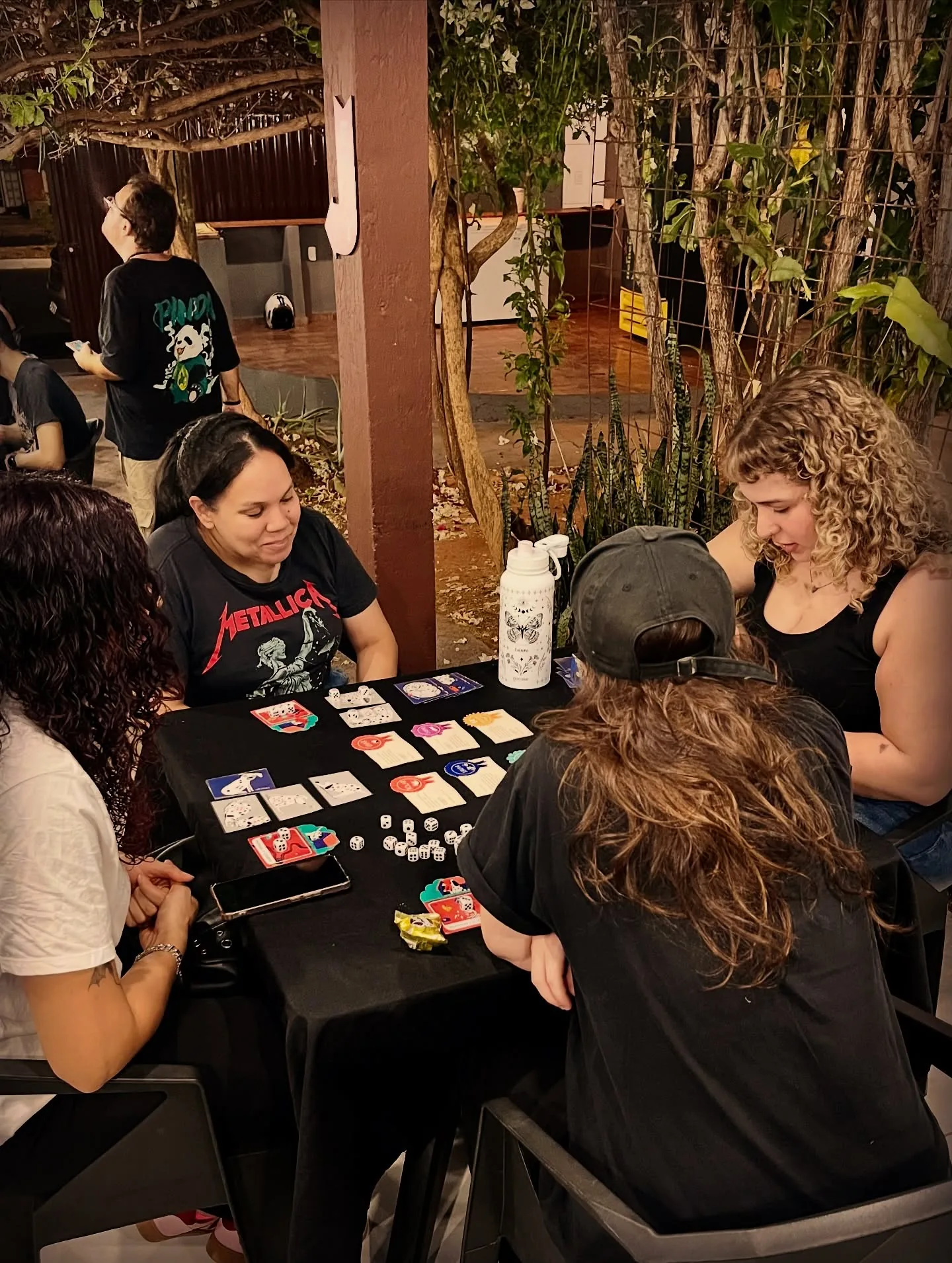 Rodada de dados e cartas entre amigas, com plantas ao fundo