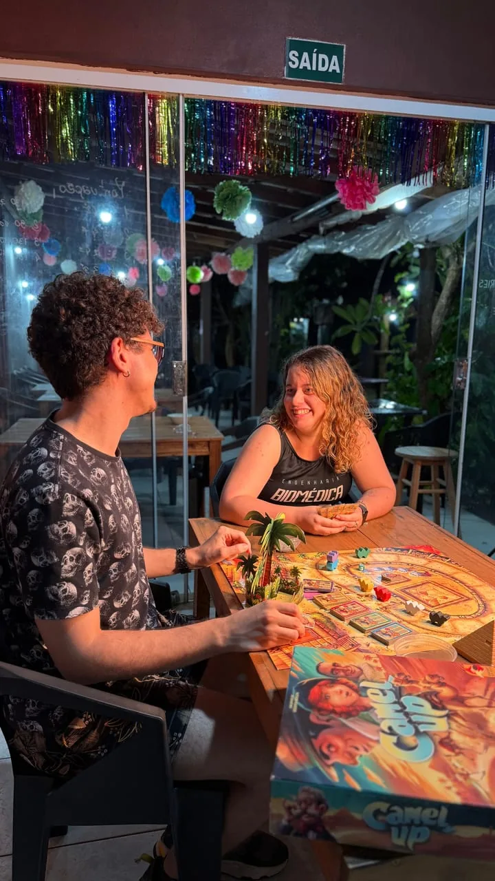 Casal jogando Camel Up numa mesa do pátio, rindo à noite