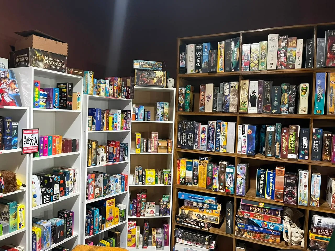 Parede de estantes do chão ao teto, lotada de caixas de jogos de tabuleiro
